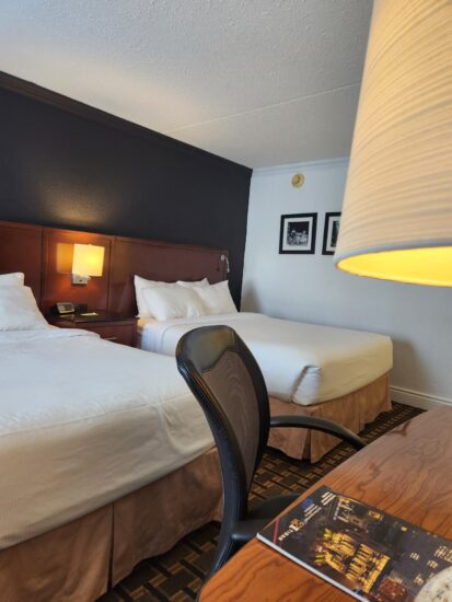 Cozy hotel room with two Queen beds, warm lighting, and a modern workspace – perfect for relaxation and productivity.