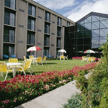 Terrasse ensoleillée à l’arrière de l’hôtel La Saguenéenne, offrant un espace relaxant avec des tables, chaises,