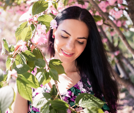 femme souriante aux cheveux bruns, photographiée parmi les branches de cerisier en fleurs au printemps